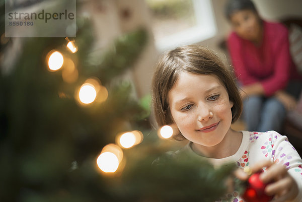 Ein Mädchen  das einen handgemachten Schmuck an einem Weihnachtsbaum platziert.