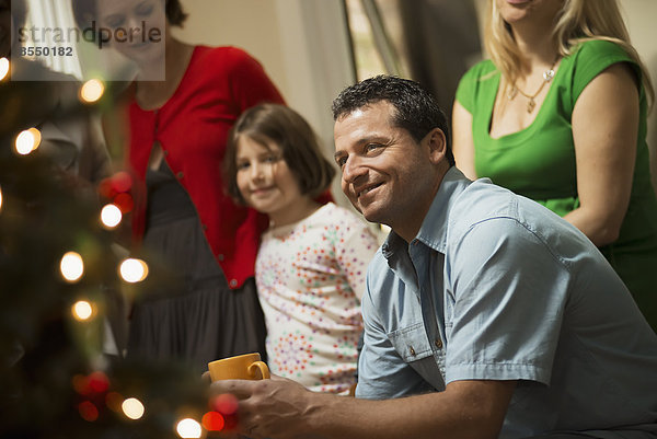 Eine weihnachtliche Versammlung  Erwachsene und Kinder in einem Raum um einen Weihnachtsbaum  die gemeinsam feiern.