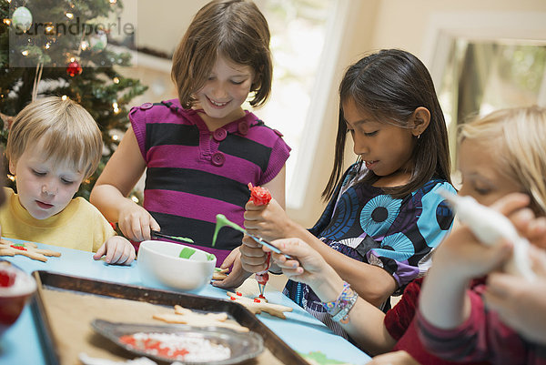 Eine Gruppe von Kindern  Mädchen und Jungen  um einen Tisch herum  schmückt Bio-Weihnachtsplätzchen.