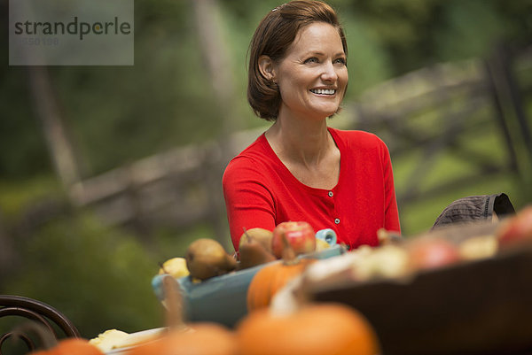 Eine Frau im roten Hemd  an einem Erntetisch im Freien.