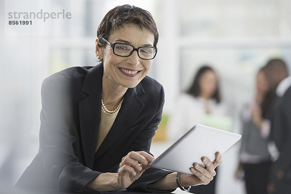 Eine Büroeinrichtung. Eine Frau in einer schwarzen Jacke  die ein digitales Tablett benutzt.