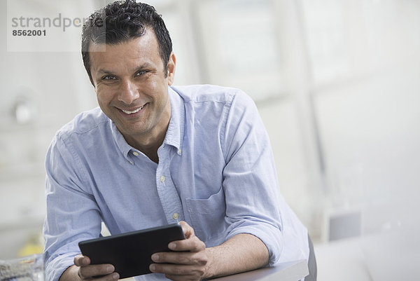 Ein Mann in einem blauen Hemd lehnt auf einem Schreibtisch und hält ein digitales Tablett.