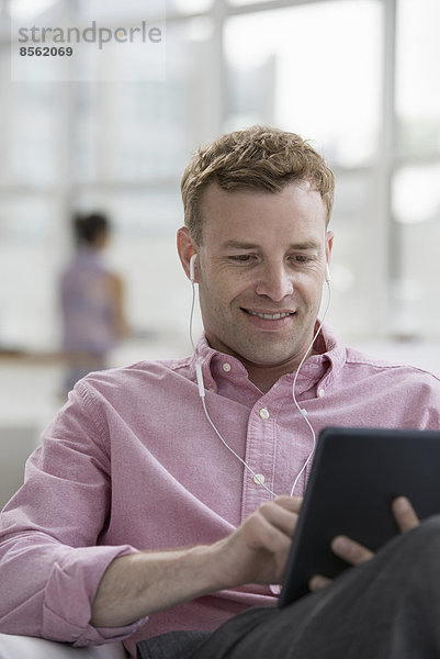 Ein Großraumbüro in New York City. Ein Mann in einem rosa Hemd sitzt lächelnd und benutzt ein digitales Tablet.