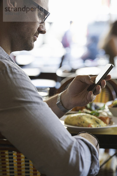 Unterwegs in Kontakt bleiben. Ein Mann in legerer Kleidung sitzt an einem Cafétisch und überprüft sein Smartphone.
