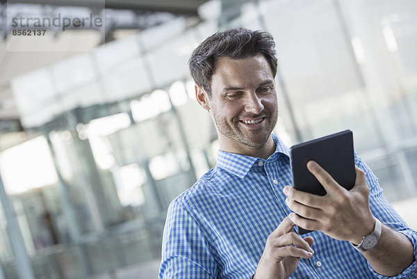 Geschäftsleute in der Stadt. Unterwegs in Kontakt bleiben. Ein Mann in einem blauen Hemd mit einem digitalen Tablet.