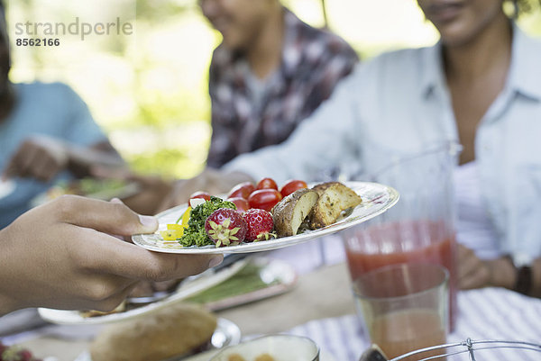 Ein Familienpicknick in einem schattigen Waldgebiet. Erwachsene und Kinder sitzen an einem Tisch.