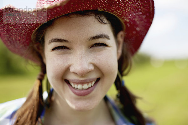 Eine junge Frau mit einem rosa Strohhut  die breit lächelt.
