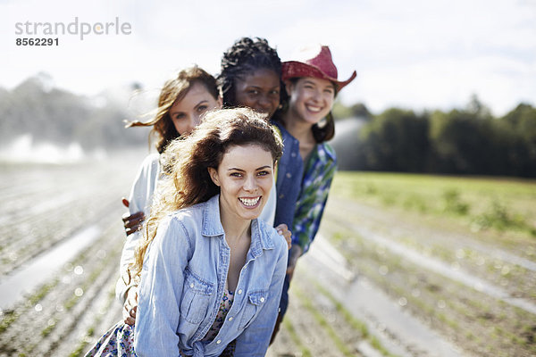 Vier junge Frauen auf einem Feld voller Setzlinge  einer Bio-Kulturpflanze  mit Sprinklern  die im Hintergrund Wasser versprühen.