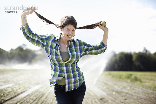 Ein Mädchen in einem grün karierten Hemd mit Zöpfen steht in einem Feld mit Sprinklern  die im Hintergrund arbeiten.