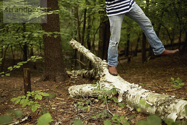 Ein Mann geht im Wald an einem umgefallenen Baumstamm entlang und balanciert mit einem Bein in die Luft erhoben.
