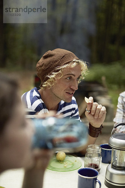 Ein junger Mann sitzt an einem Picknicktisch im Wald.