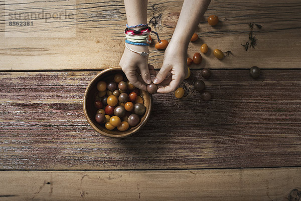 Eine runde Schüssel mit kleinen Tomaten in verschiedenen Farben  die von einer Person sortiert und gepflückt werden. Eine Tischplatte aus Holz.