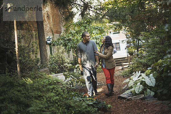 Szenen aus dem städtischen Leben in New York City. Ein Mann und eine Frau  ein Paar beim Spaziergang durch den Park  durch einen begrünten Raum mit Bäumen und grünem Laub und einer Bank.