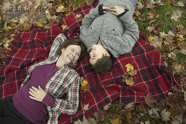 Zwei Personen  eine Frau und ein Kind  liegen auf einer roten Schottenkaro-Picknickdecke und schauen nach oben.