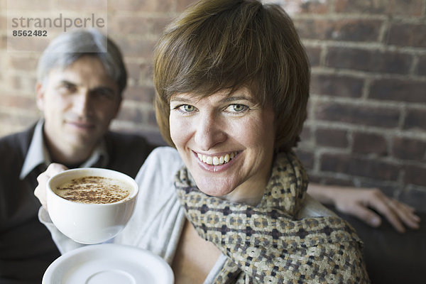 Zwei Personen sitzen in einem Café. Ein Mann und eine Frau  die weiße Porzellantassen mit Cappuccino-Kaffee in der Hand halten.