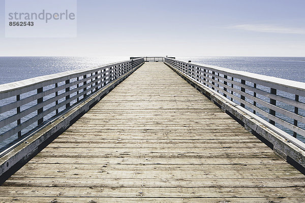 Ein langer Pier mit einem Geländer  das sich über den Pazifischen Ozean bis zum Horizont erstreckt.