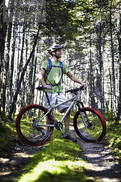 Ein Mountainbiker mit Helm und Rucksack steht im Wald an seinem Fahrrad.