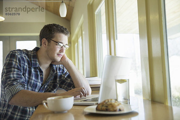 Ein junger Mann sitzt an einem Tisch mit einem Laptop-Computer.