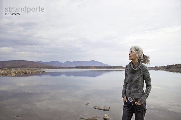 Eine Frau  die am Ufer eines ruhigen Sees über das Wasser schaut.