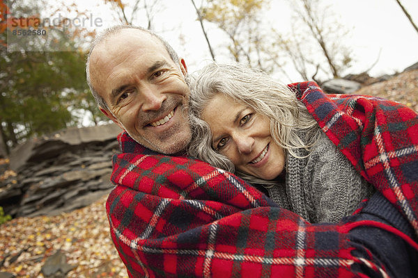 Ein Paar  Mann und Frau an einem Ausflugstag im Herbst. Sie teilen sich eine Picknickdecke  um sich warm zu halten.