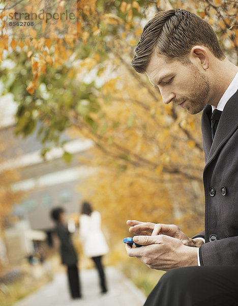 Stadtleben. Ein Mann im Park kontrolliert und schreibt SMS  hält Kontakt  benutzt ein Mobiltelefon.
