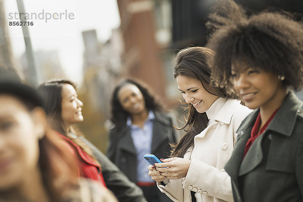 Stadtleben. Eine Gruppe von Menschen  die unterwegs ist  in Kontakt bleibt  Mobiltelefone benutzt und miteinander spricht. Fünf Frauen.