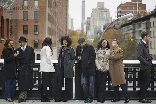Stadtleben. Eine Gruppe von Menschen  die unterwegs ist  in Kontakt bleibt  Mobiltelefone benutzt und miteinander spricht. In einer Schlange stehen.
