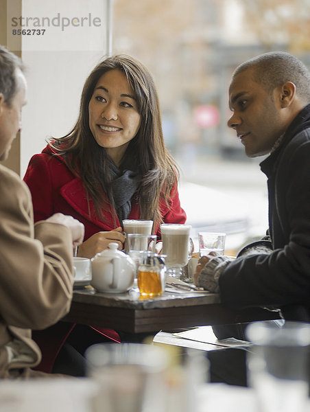 Stadtleben. Eine Gruppe von Menschen unterwegs. Drei Menschen in einem Café  die an einem Tisch sitzen und miteinander reden.