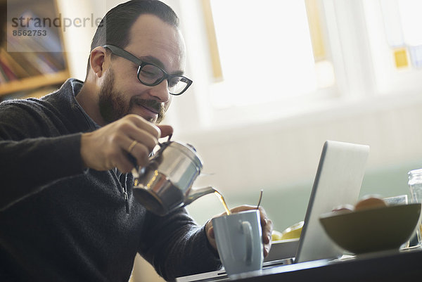 Ein bärtiger Mann beim Kaffeetrinken. Ein offener Laptop-Computer auf der Theke.