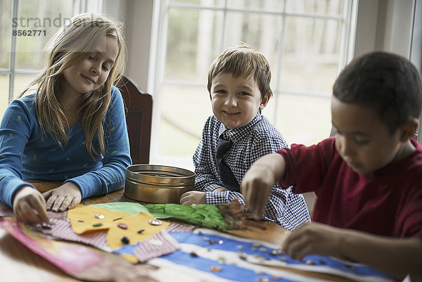 Kinder in einem Familienhaus. Drei Kinder basteln Bilder  mit Kleber und Aufklebern. Kunsthandwerk.