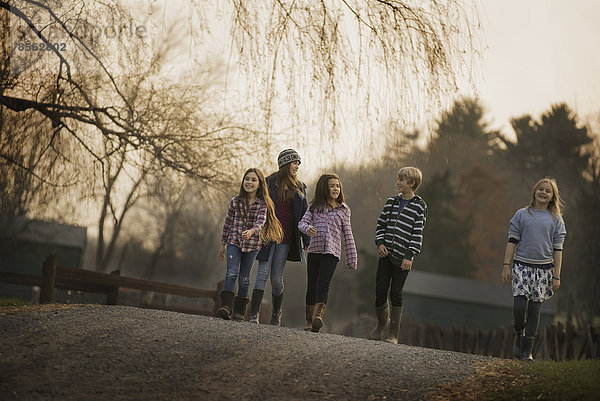 Eine Gruppe von Kindern  ein Junge und vier Mädchen  die an einem Wintertag einen Weg entlanglaufen. Ein Bio-Bauernhof.