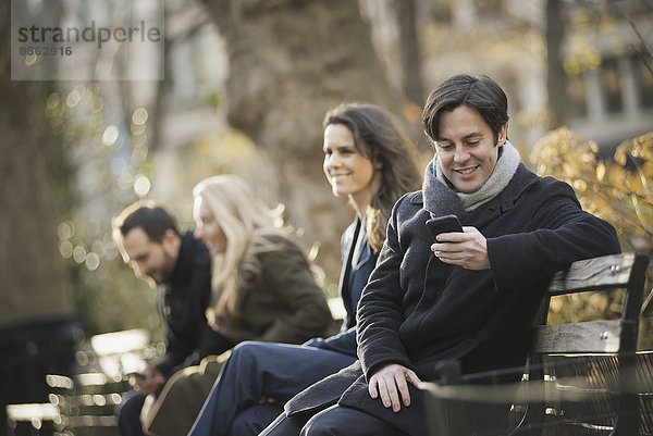 Gruppe auf Bank im Stadtpark mit Smartphones