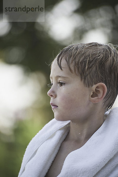 Ein kleiner Junge mit nassem Haar  nach dem Schwimmen in ein Handtuch gewickelt.