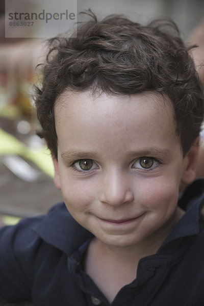 Ein kleiner Junge mit dunklem Haar und braunen Augen  der nach oben schaut und lächelt.