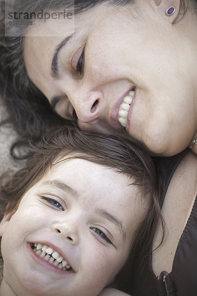 Die Nahaufnahme einer Mutter und einer Tochter  die lächelnd und lachend mit dem Kopf zusammen liegen.