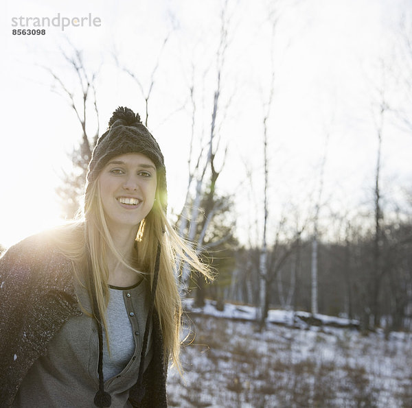 Eine junge Frau mit blonden Haaren und einer gestrickten Wollmütze und einem Wollmantel. Draußen an einem Wintertag. Schnee auf dem Boden.