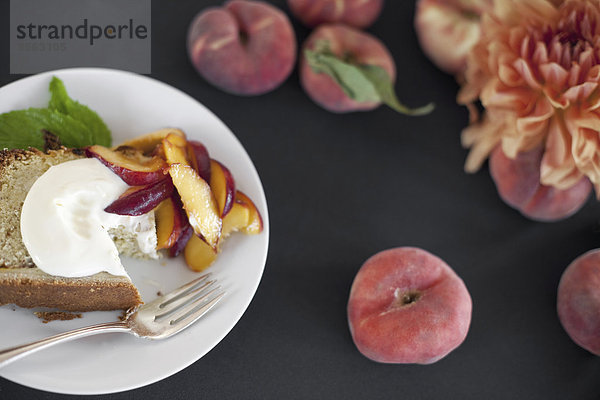 Eine Tabelle von oben betrachtet. Bio-Obst  Pfirsiche und Blumen. Ein Teller mit frischem Obst  Kuchen und Crème fraîche. Eine Gabel. Ein Dessert.