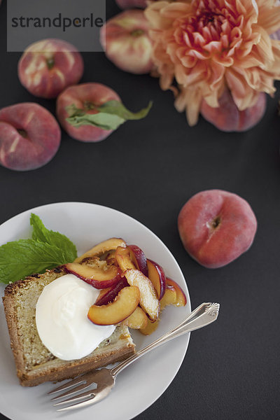 Eine Tabelle von oben betrachtet. Bio-Obst  Pfirsiche und Blumen. Ein Teller mit frischem Obst  Kuchen und Crème fraîche. Eine Gabel. Ein Dessert.