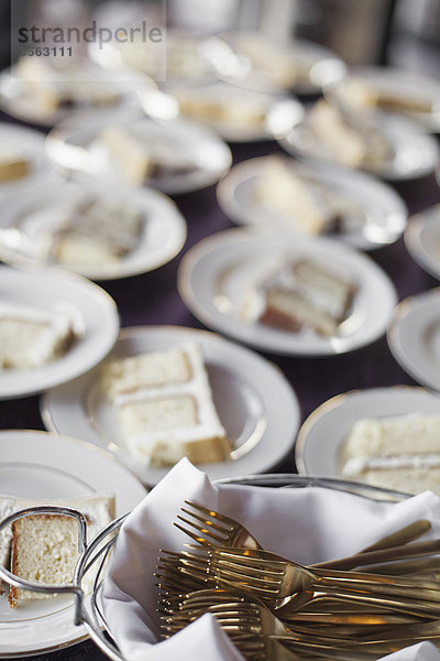 Ein mit Tellern beladener Tisch. Weißes Porzellan und ein Korb voller Dessertgabeln. Ein Stück Hochzeitstorte.