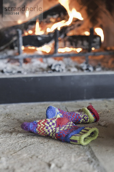 Ein Holzfeuer in einer Feuerstelle mit glühendem Herz und Flammen. Gemusterte  gestrickte Wollhandschuhe.