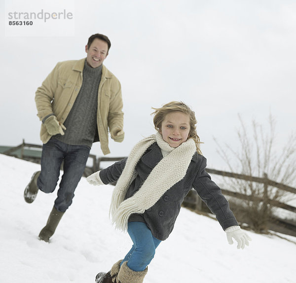 Ein Mann jagt ein junges Mädchen durch den Schnee. Bauernhof im Winter.