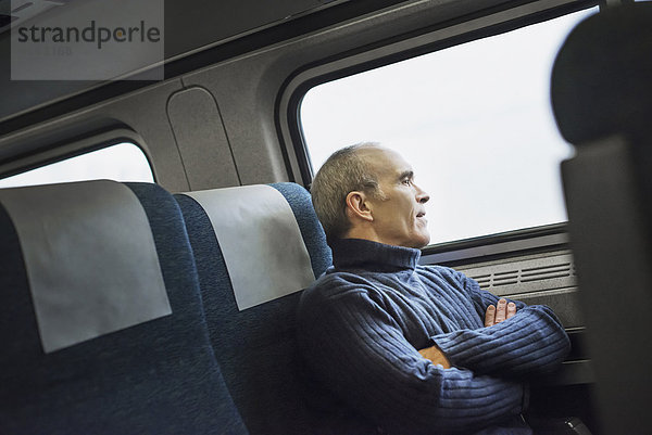 Ein reifer Mann  der auf einer Zugfahrt am Fenster sitzt und in die Ferne schaut.