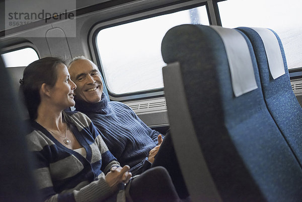 Zwei Menschen sitzen lächelnd in einem Eisenbahnwagen. Sie machen eine Zugfahrt.