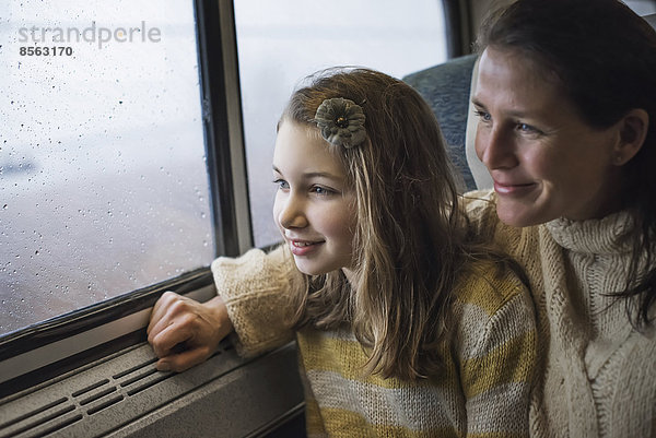 Ein Mann und ein junges Mädchen sitzen in einem Zugwaggon am Fenster und blicken auf die Landschaft. Lächeln vor Aufregung.