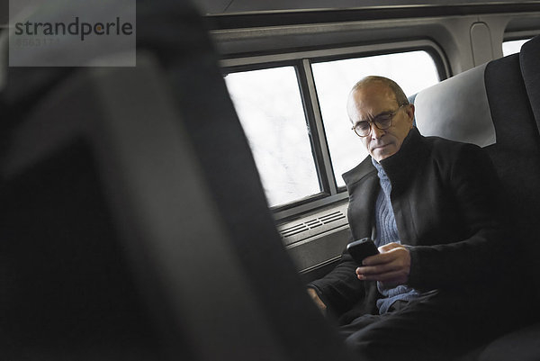 Ein reifer Mann  der in einem Zugwaggon am Fenster sitzt  sein Mobiltelefon benutzt und während der Fahrt in Kontakt bleibt.