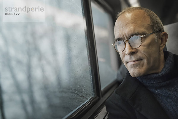 Ein reifer Mann  der auf einer Zugfahrt am Fenster sitzt und in die Ferne schaut.