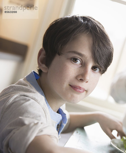 Ein Kind  ein kleiner Junge mit braunen Haaren und braunen Augen sitzt am Familientisch.