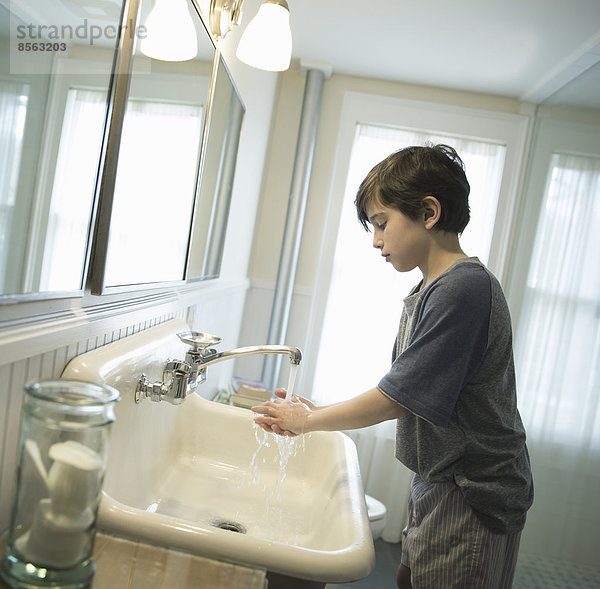 Ein Junge steht im Badezimmer und wäscht sich die Hände unter dem Wasserhahn.