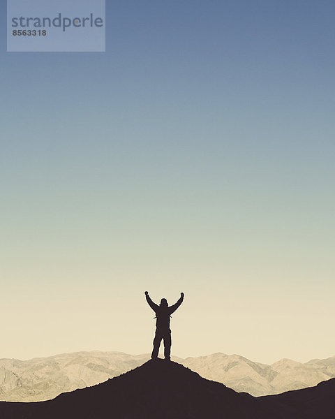 Silhouette eines männlichen Wanderers  der einen Rucksack trägt und auf einem Hügel im Death Valley Nationalpark steht.