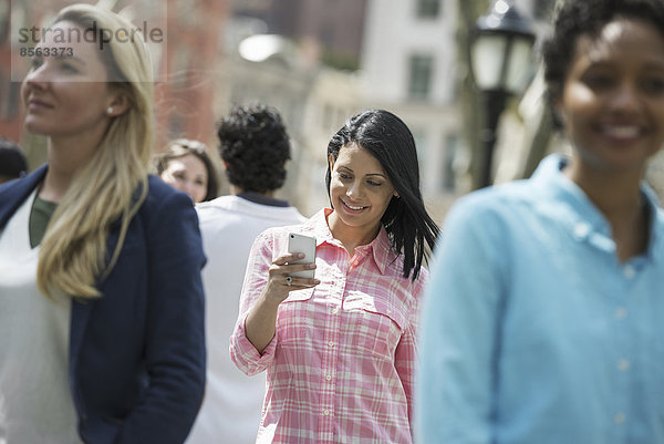 Menschen im Frühling in der Stadt im Freien. Der New Yorker Stadtpark. Drei Frauen  eine überprüft ihr Mobiltelefon.